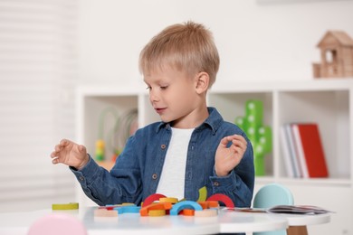 Cute little boy playing with colorful wooden pieces at white table indoors. Child's toy