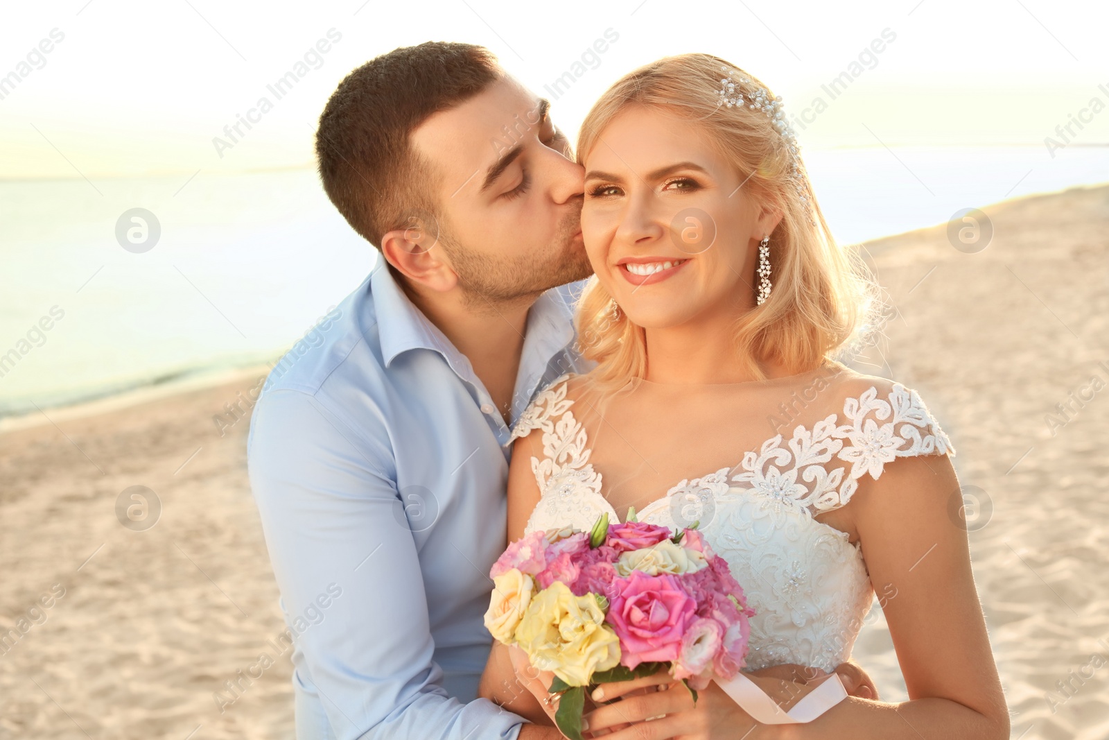 Photo of Groom hugging and kissing bride on beach. Wedding couple