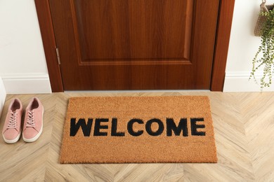 Door mat with word Welcome on wooden floor in hall