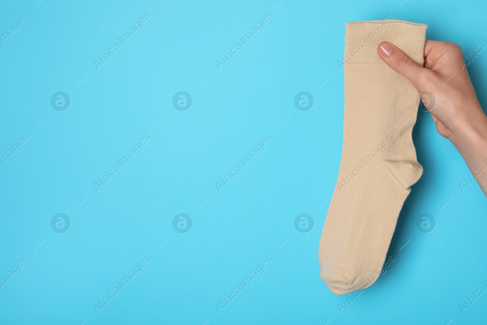 Photo of Woman holding beige sock on light blue background, closeup. Space for text