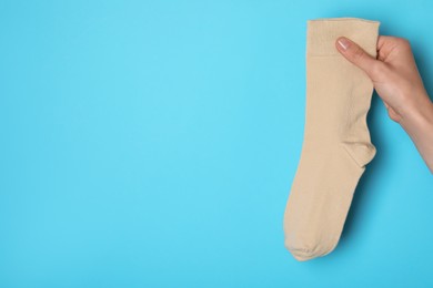 Photo of Woman holding beige sock on light blue background, closeup. Space for text