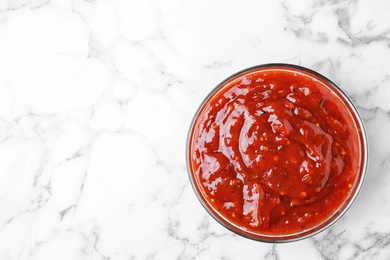 Photo of Bowl of hot chili sauce on marble background, top view. Space for text