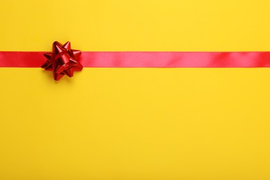 Photo of Red ribbon with bow on yellow background, top view. Space for text