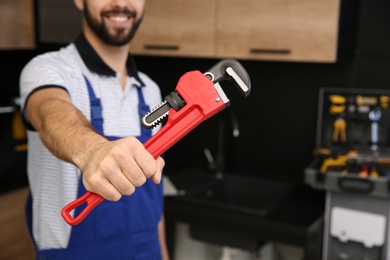 Male plumber holding pipe wrench in kitchen, closeup with space for text. Repair service