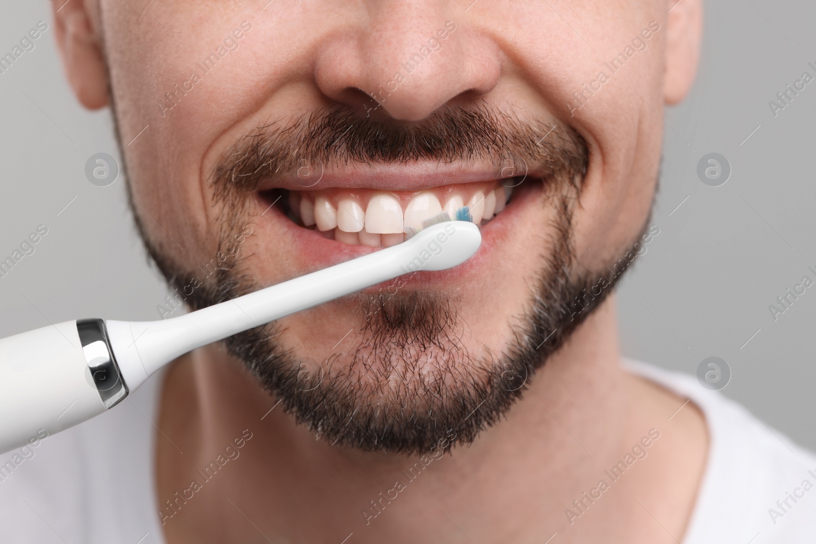 Photo of Man brushing his teeth with electric toothbrush on light grey background, closeup