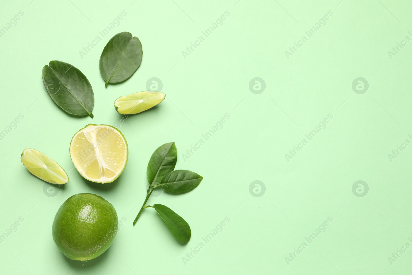 Photo of Whole and cut fresh ripe limes with leaves on light green background, flat lay