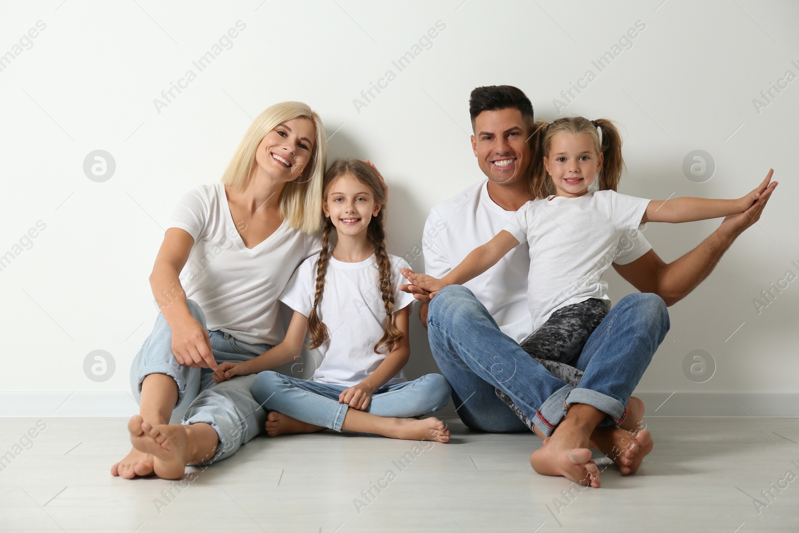 Photo of Happy family sitting on floor near white wall