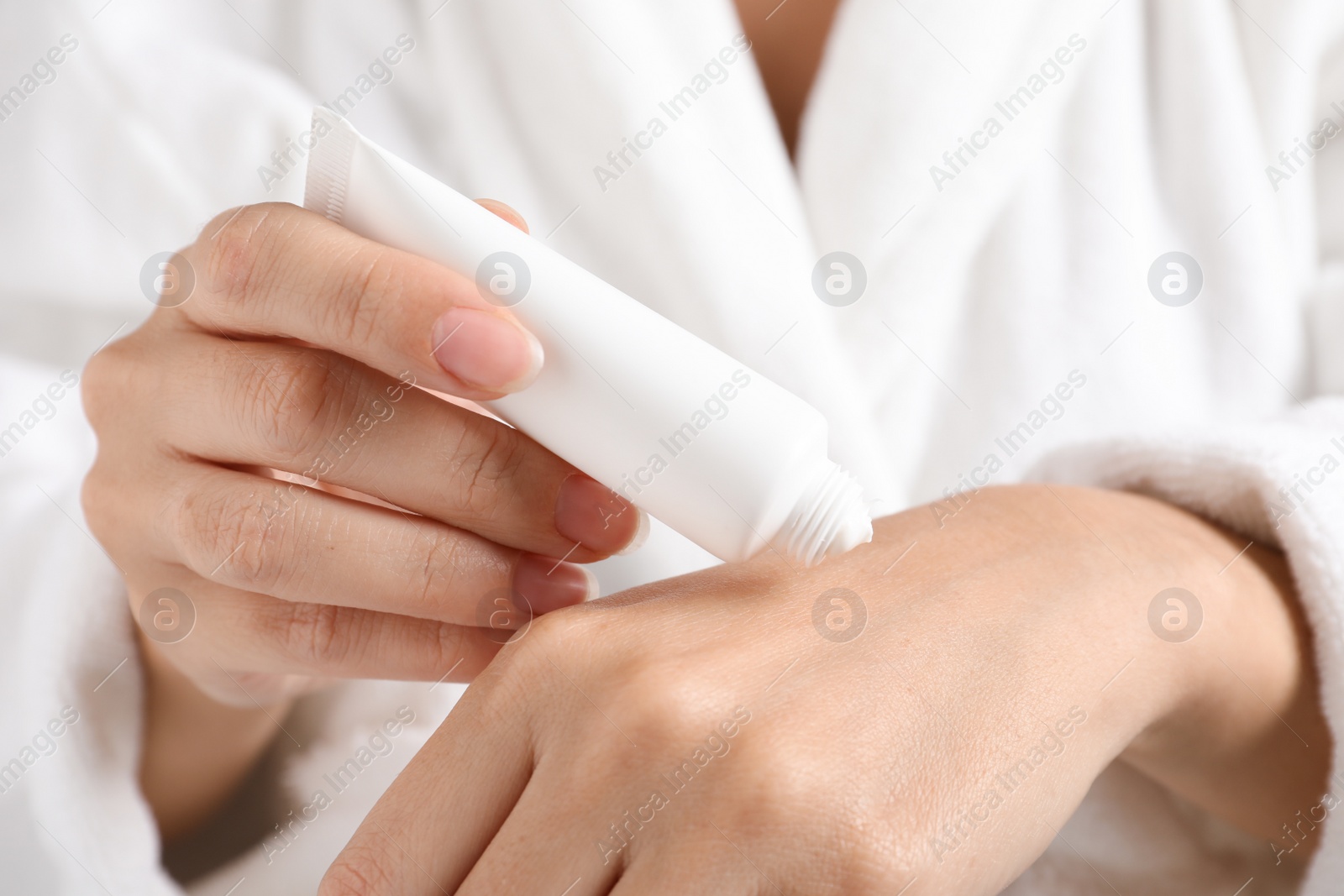 Photo of Woman in bathrobe applying moisturizing hand cream, closeup. Winter skin care cosmetic