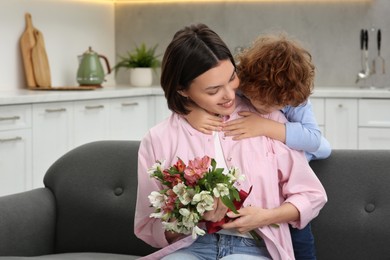 Photo of Little son congratulating his mom with Mother`s day at home. Woman holding bouquet of flowers