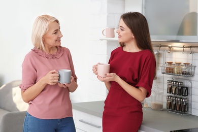 Portrait of mature woman and her daughter drinking tea in kitchen