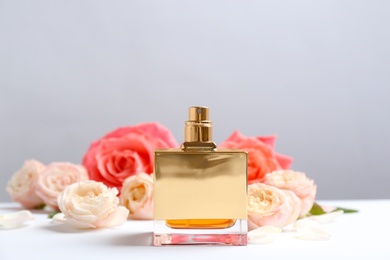 Photo of Bottle of perfume with beautiful roses on table