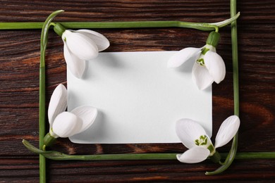 Photo of Beautiful snowdrops and paper card on wooden table, flat lay with space for text