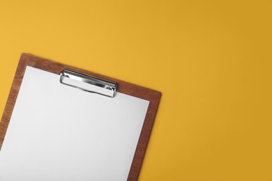 Photo of Wooden clipboard with sheet of blank paper on yellow background, top view. Space for text