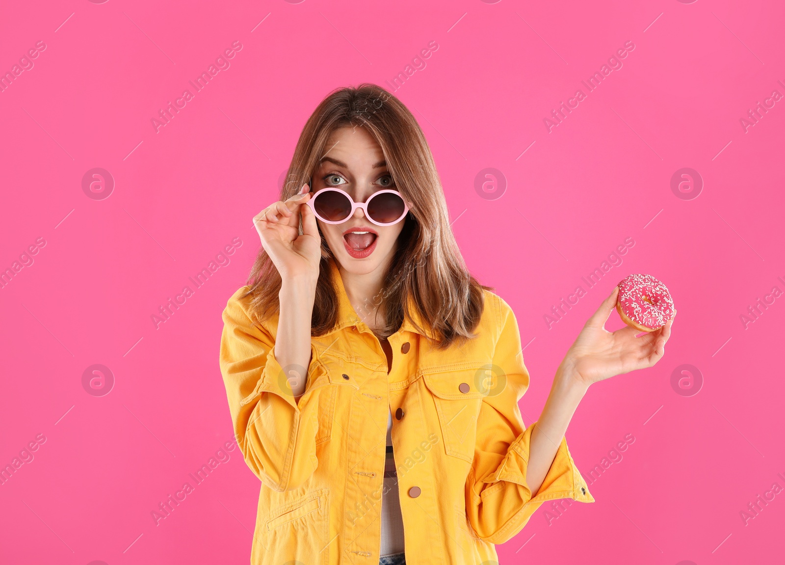 Photo of Beautiful young woman wearing sunglasses with donut on pink background