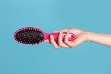 Photo of Woman holding hair brush against blue background, closeup