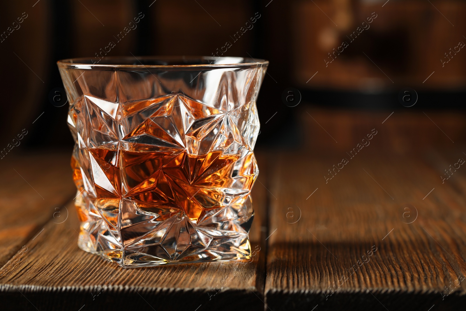 Photo of Glass of tasty whiskey on wooden table, closeup. Space for text