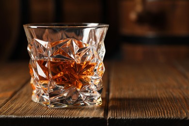 Photo of Glass of tasty whiskey on wooden table, closeup. Space for text