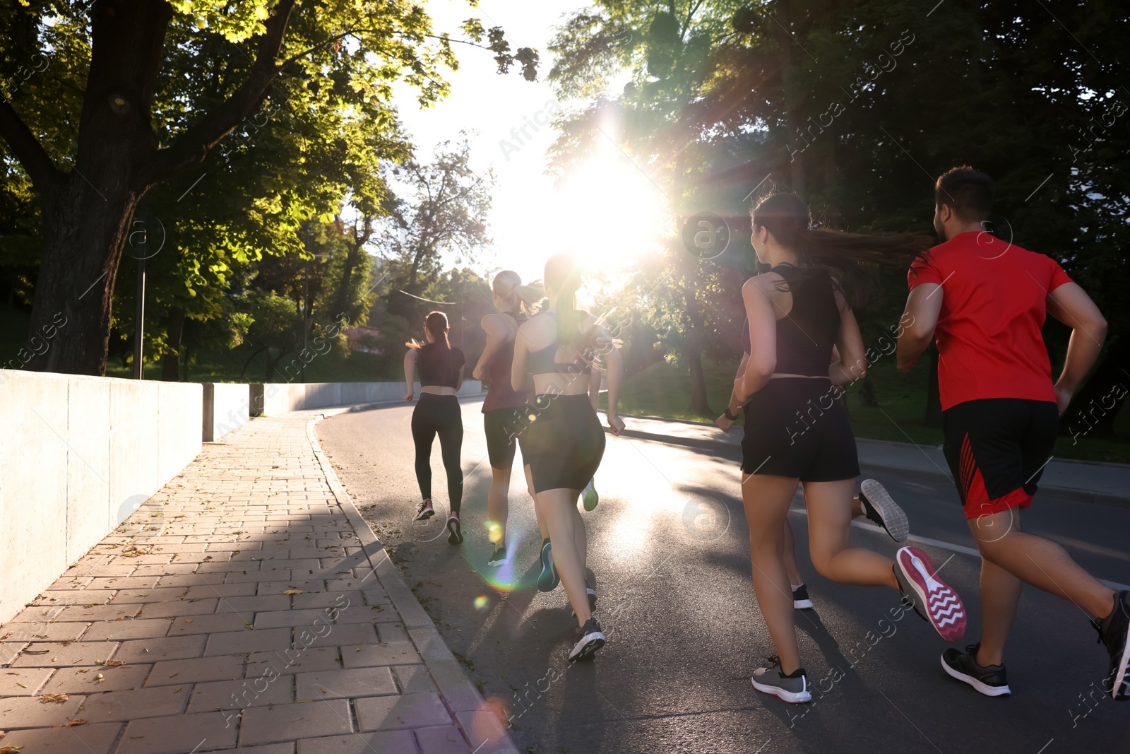 Photo of Group of people running outdoors on sunny day, back view