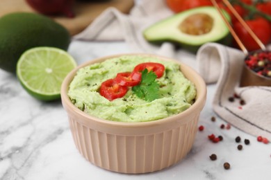 Bowl of delicious guacamole and ingredients on white marble table, closeup