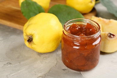 Photo of Delicious quince jam and fruits on light grey table, closeup
