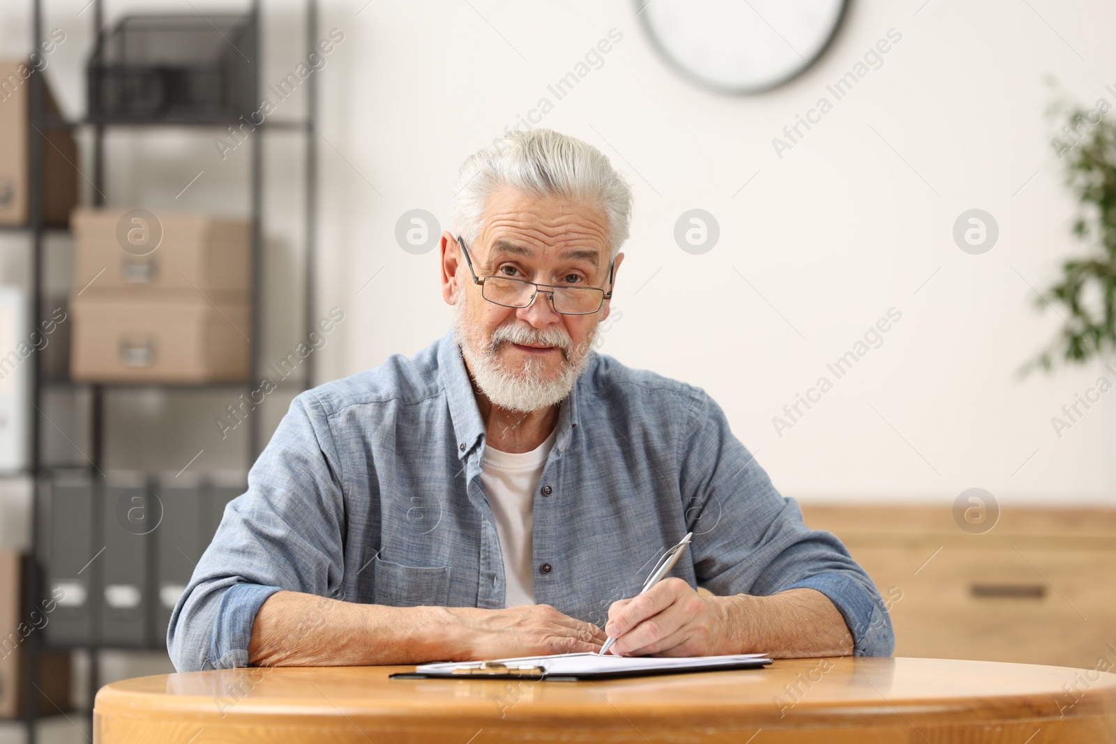 Photo of Senior man signing Last Will and Testament at table indoors