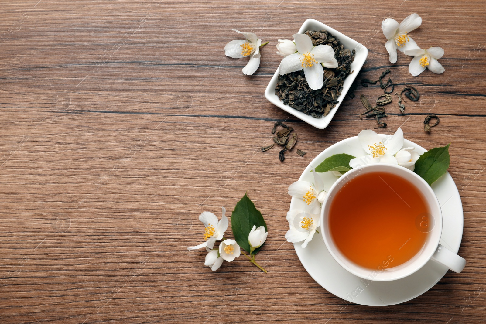 Photo of Cup of aromatic jasmine tea, dry leaves and fresh flowers on wooden table, flat lay. Space for text