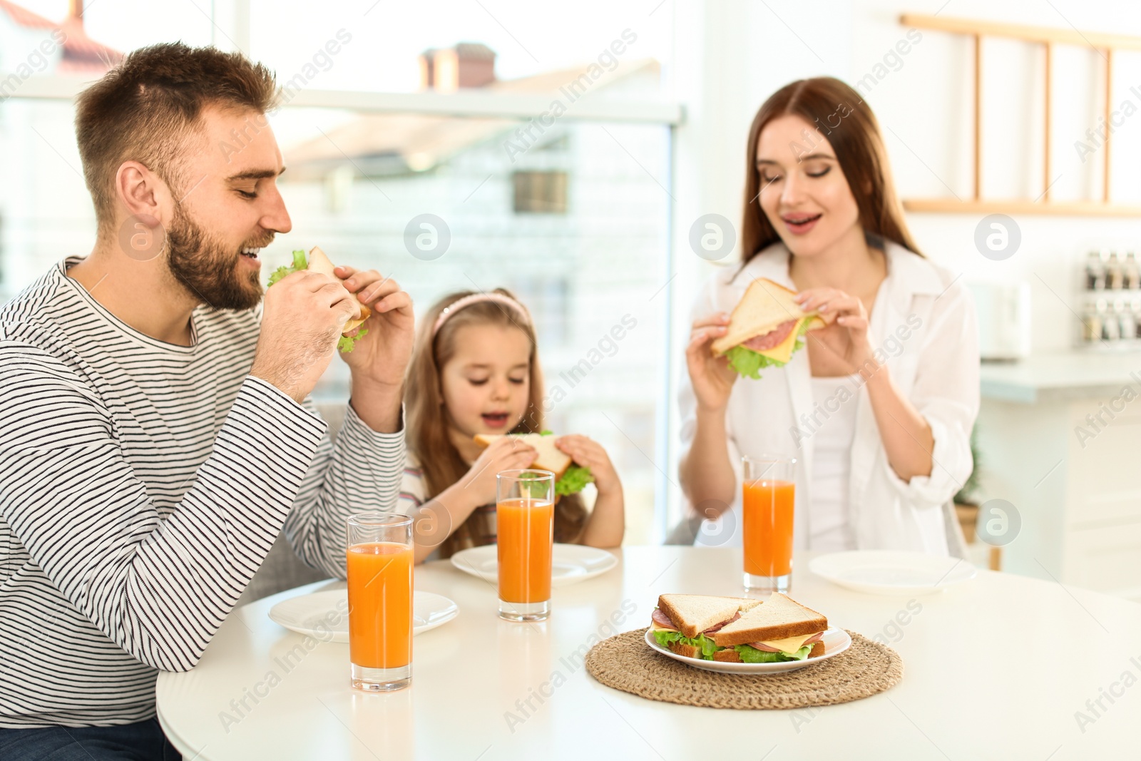 Photo of Happy family having breakfast with sandwiches at table in kitchen