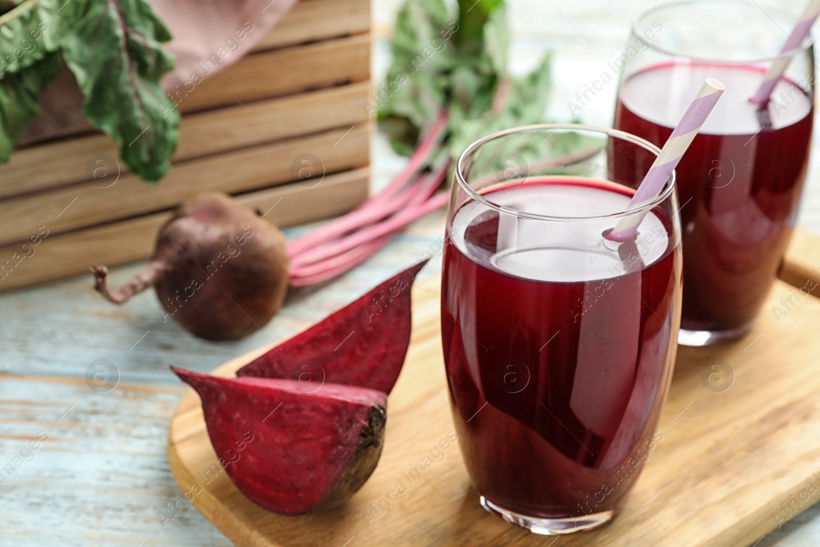 Photo of Wooden board with cut beet and glasses of juice on table. Space for text