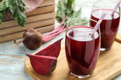 Photo of Wooden board with cut beet and glasses of juice on table. Space for text