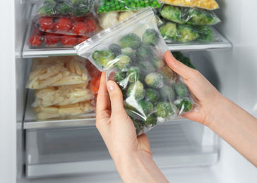Photo of Woman holding plastic bag with frozen brussels sprouts near open refrigerator, closeup