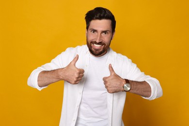 Photo of Handsome bearded man showing thumbs up on orange background