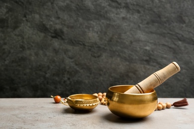 Photo of Golden singing bowl with mallet on grey table against dark background, space for text. Sound healing