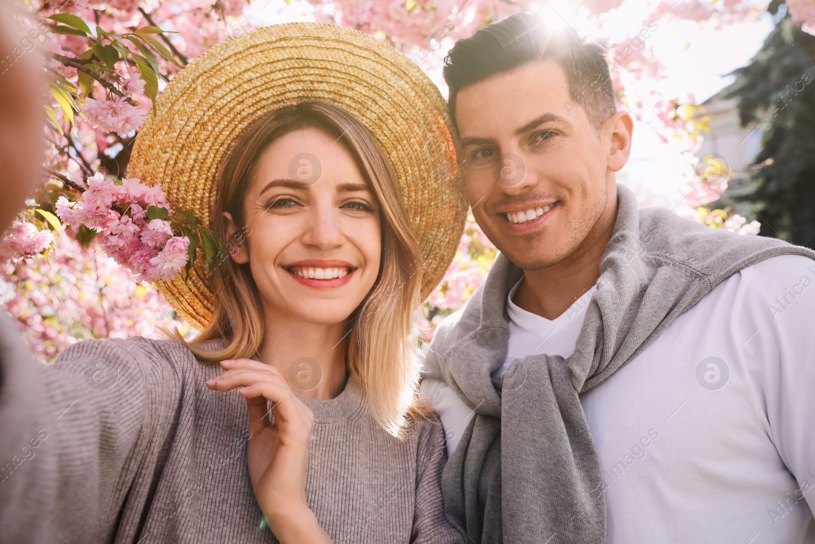 Photo of Happy couple taking selfie near blossoming sakura outdoors on spring day