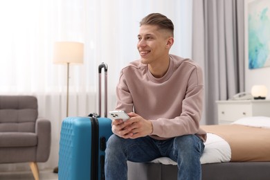 Smiling guest with smartphone relaxing on bed in stylish hotel room