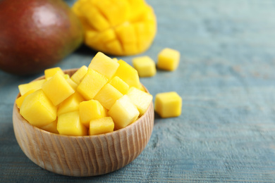 Cubes of fresh ripe mango in bowl on wooden table. Space for text