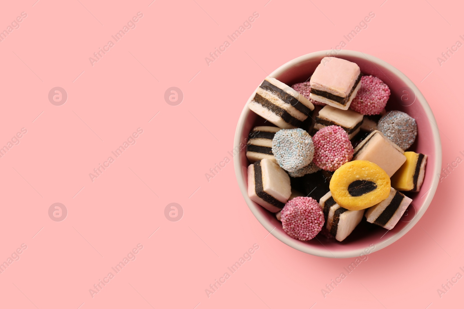 Photo of Bowl of tasty liquorice candies on pink background, top view. Space for text