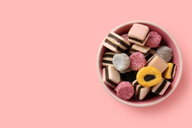 Bowl of tasty liquorice candies on pink background, top view. Space for text