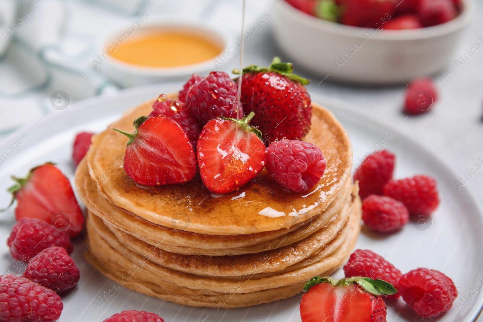 Photo of Pouring honey onto tasty pancakes with fresh berries on plate, closeup