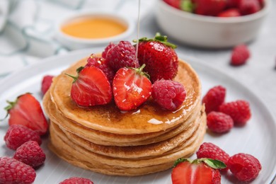 Pouring honey onto tasty pancakes with fresh berries on plate, closeup