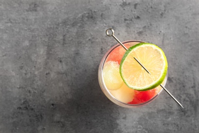 Photo of Glass of melon and watermelon ball cocktail with lime on grey table, top view. Space for text