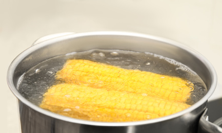 Pot with boiling corn in kitchen, closeup