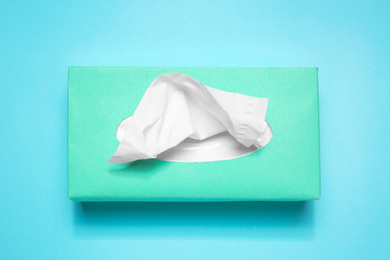 Box with paper tissues on light blue background, top view