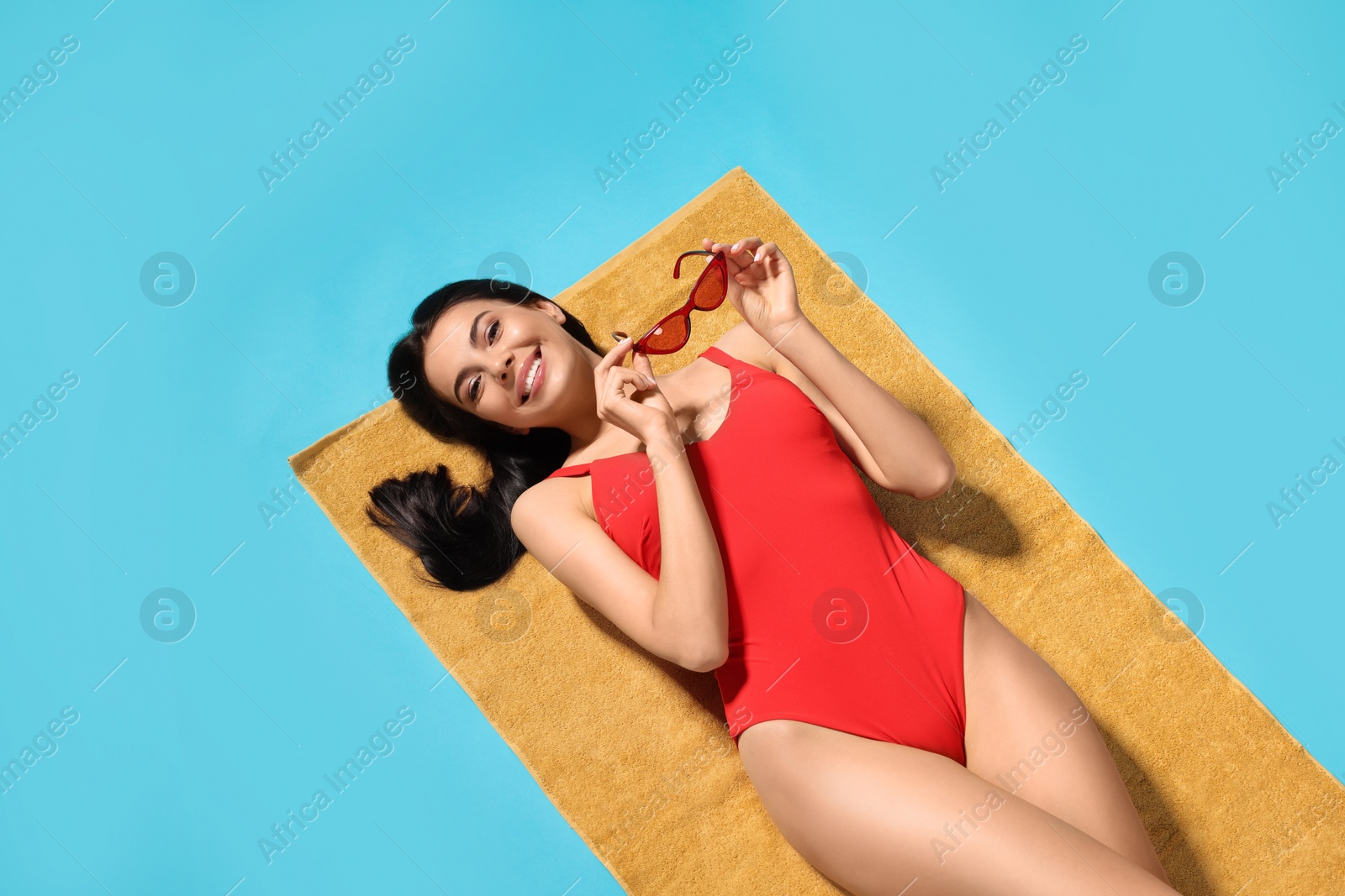 Photo of Young woman in stylish swimsuit on beach towel against light blue background