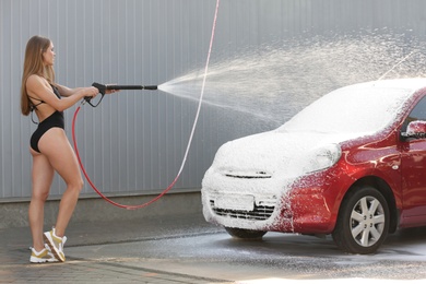 Photo of Young woman in swimsuit with high pressure water jet cleaning automobile at car wash