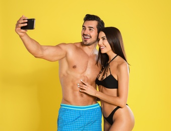 Young attractive couple in beachwear taking selfie on yellow background