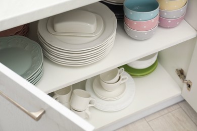 Clean plates, bowls and cups on shelves in cabinet indoors