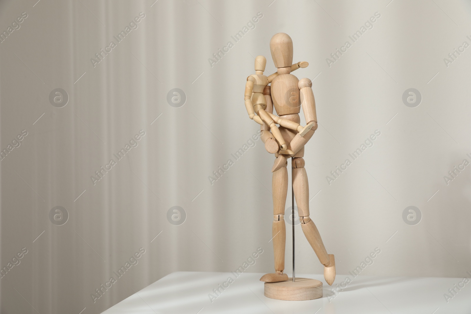 Photo of Wooden mannequins of parent with child on white table against light background, space for text. Family Day