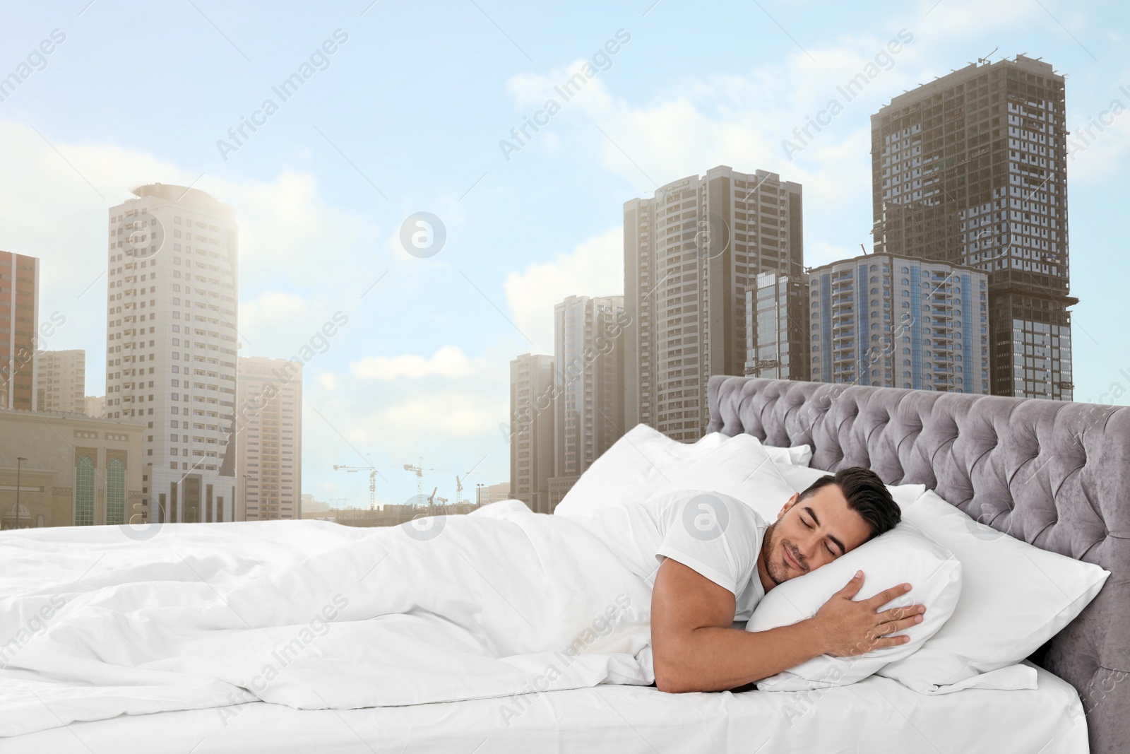 Image of Man sleeping on bed with soft pillows and beautiful view of cityscape on background. Good sleep despite of urban bustle