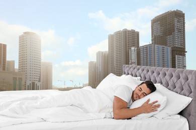 Man sleeping on bed with soft pillows and beautiful view of cityscape on background. Good sleep despite of urban bustle