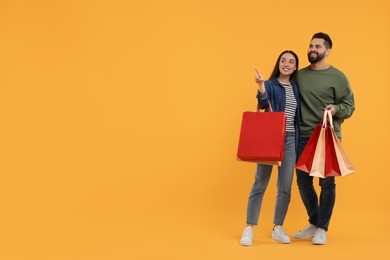 Photo of Happy couple with shopping bags looking at something on orange background. Space for text